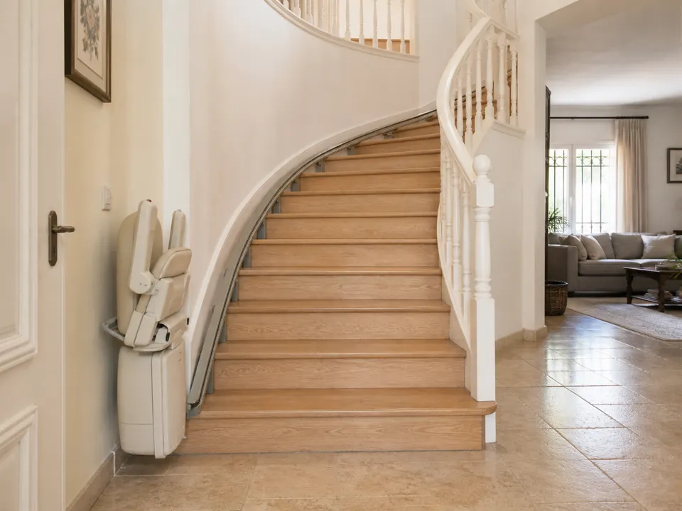 Silla salvaescaleras al pie de la escalera con curva de un chalet de dos plantas.