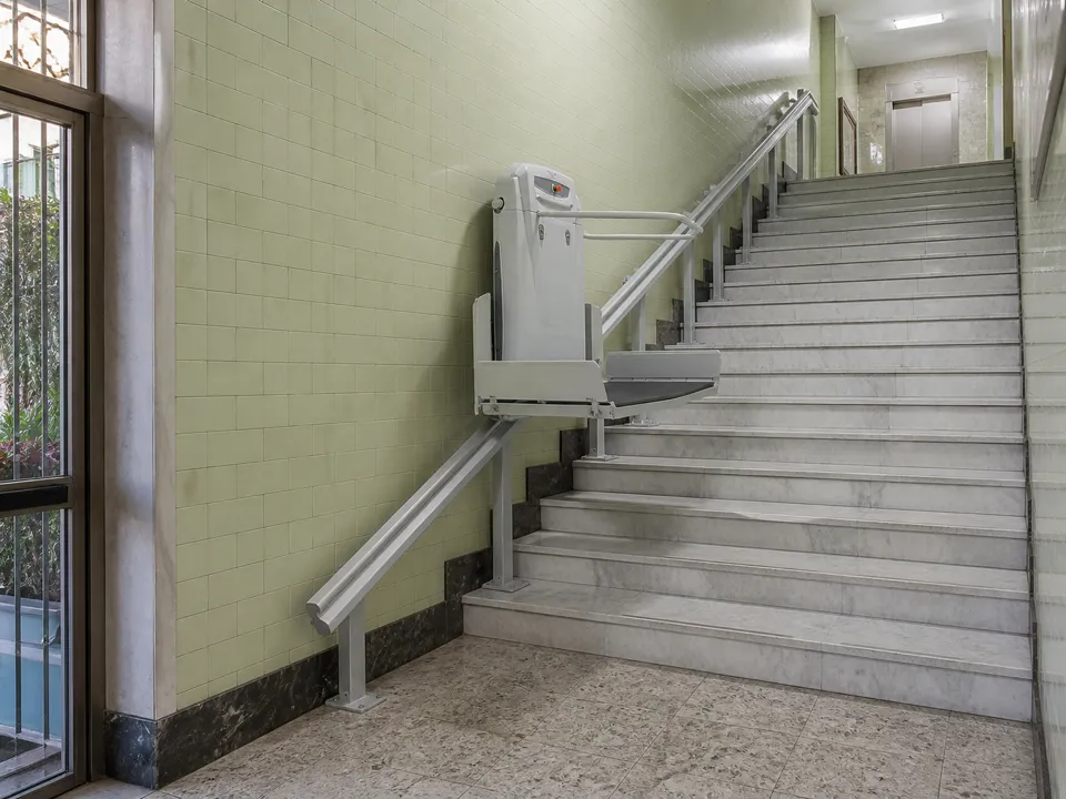 Plataforma salvaescaleras subiendo por su raíl los escalones del portal de un bloque de vecinos.